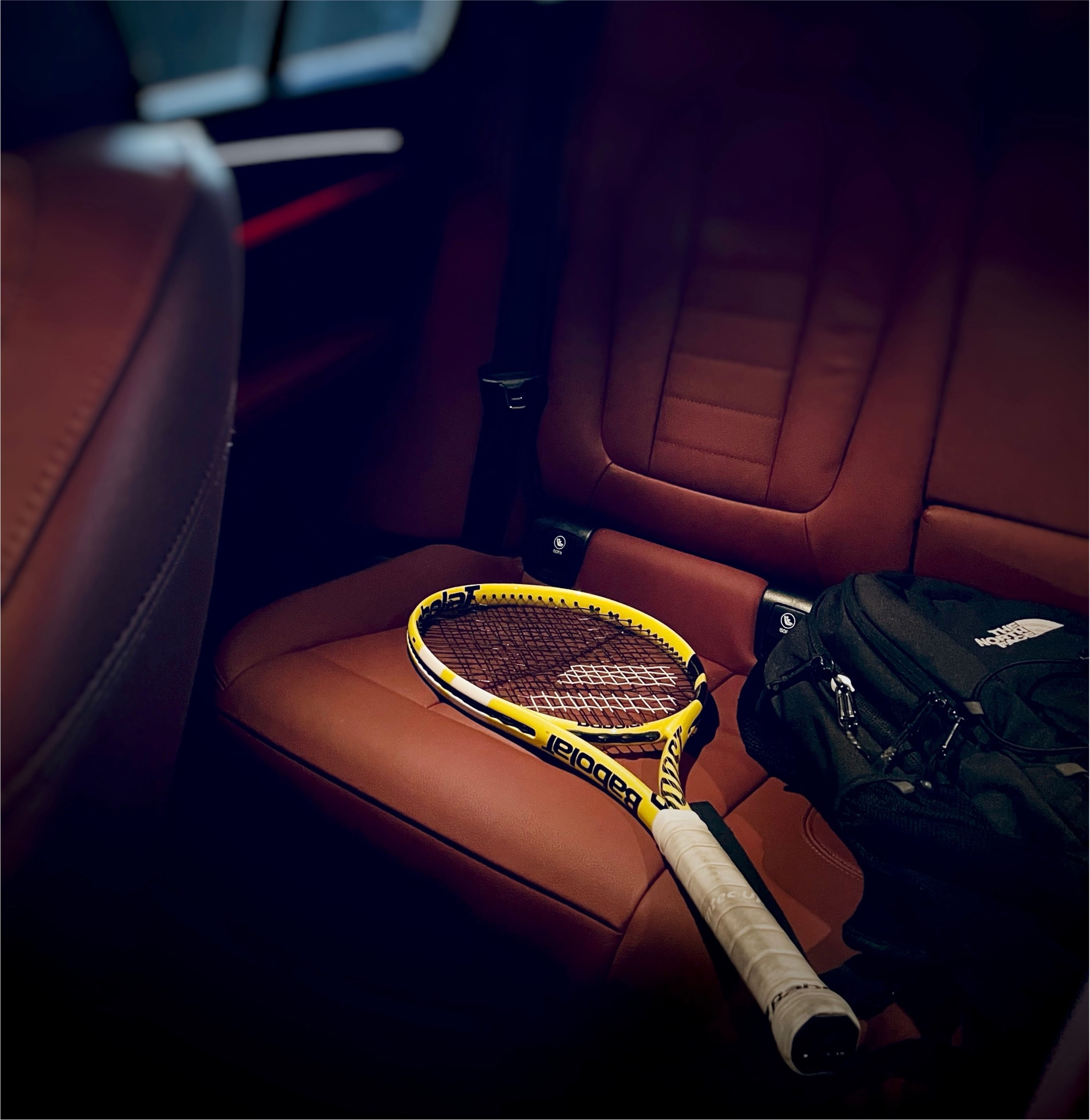 A yellow Babolat tennis racket and a black North Face backpack resting on the cognac-leather rear seat of a BMW iX — the kind of cabin scene Smart Objects was built to detect.