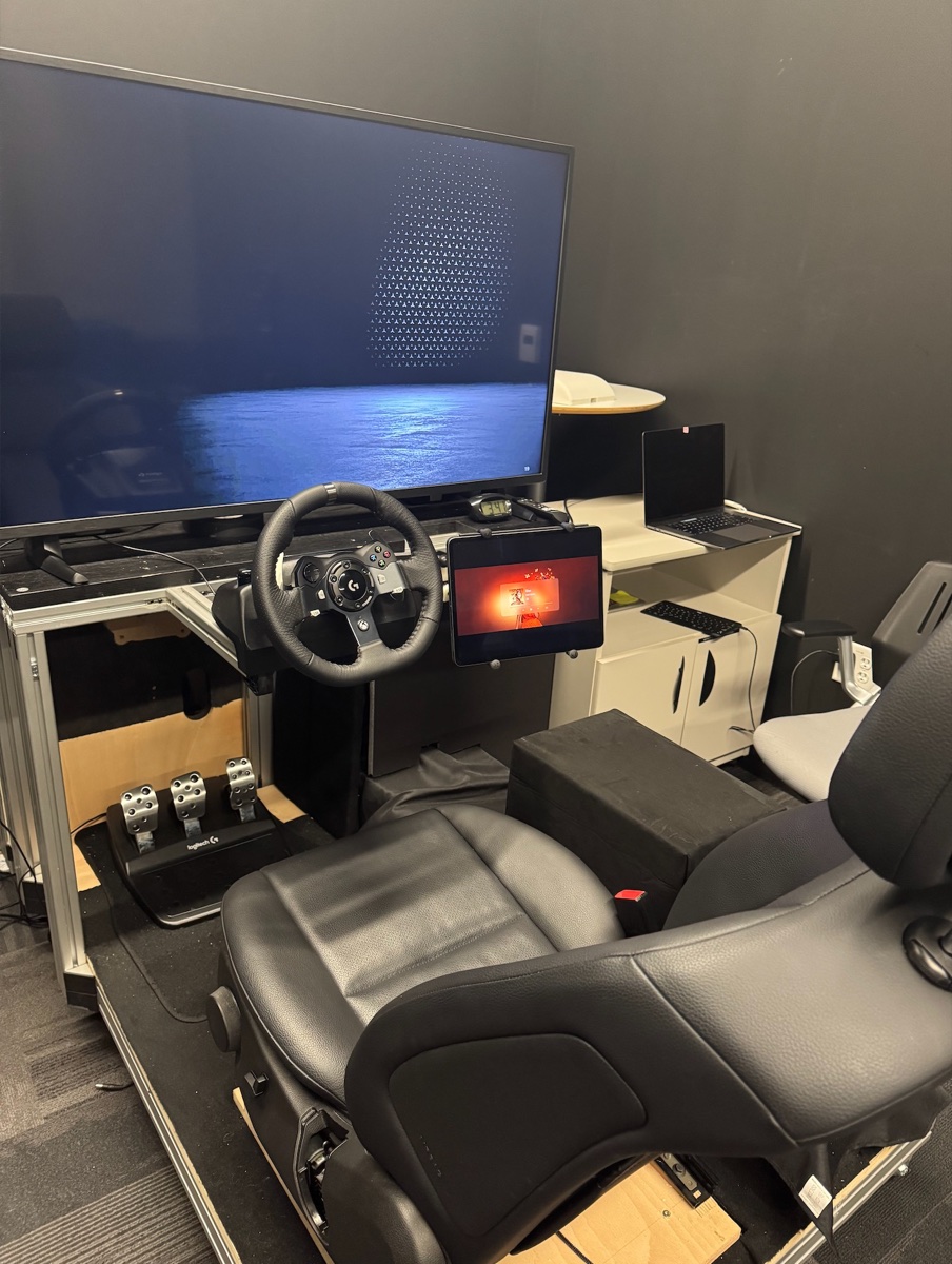 The cabin-buck study rig — a driving-sim seat and steering wheel facing a display showing a generated ocean background, with an iPad prototype on the console.