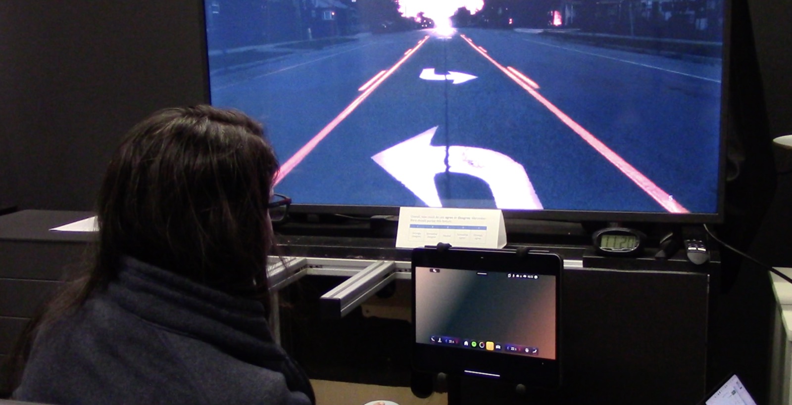 Lab driving sim — left-turn arrow on a projected road scene with the test tablet below.