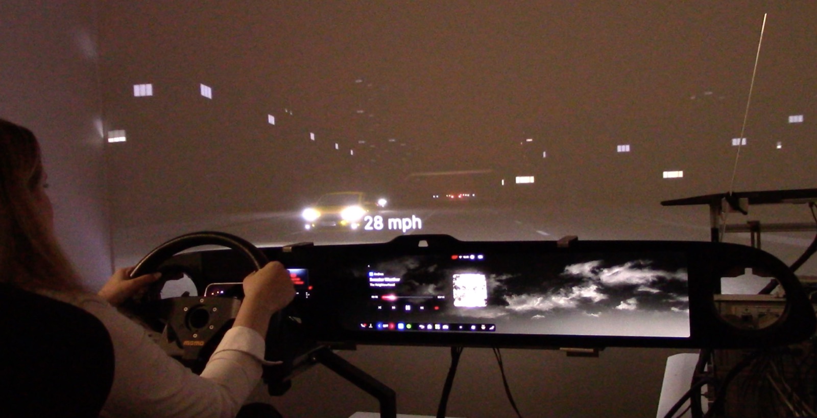 Driver at the seat-buck wheel with a night-driving sim projected on the wraparound display.