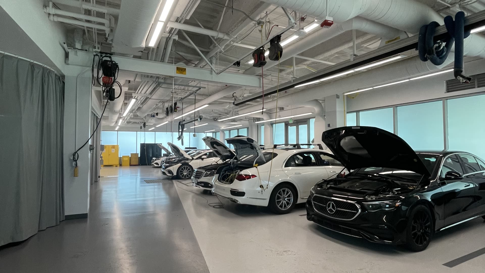 Mercedes R&D garage in Sunnyvale — a row of E-Class and S-Class dev cars with their hoods open under industrial ducting.